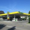 AGROLA Tankstelle in Rüti mit TopShop; im Vordergrund Strasse; Tankstelle mit Totem-Schild zuüberst AGROLA Logo, darunter digitale Preisanzeige Treibstoff