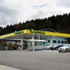 AGROLA Tankstelle in Elsau, mit TopShop, grosser Vorplatz, türkis-farbenes Gebäude hinter Tankstelle; rechts Autos geparkt