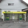 AGROLA Tankstelle in Menzingen. Zwei Tanksäulen mit Zahlterminal unter kleinem Vorstand. Im Hintergrund Gebäude mit grauer Fassade.