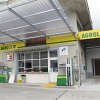 AGROLA Tankstelle in Gersau unter Wellblechdach; zwei Tanksäulen; Spitex Logo an Fassade über Tanksäule; Fensterfront und Tür zwischen Säulen it Blumentöpfen auf Fensterfront